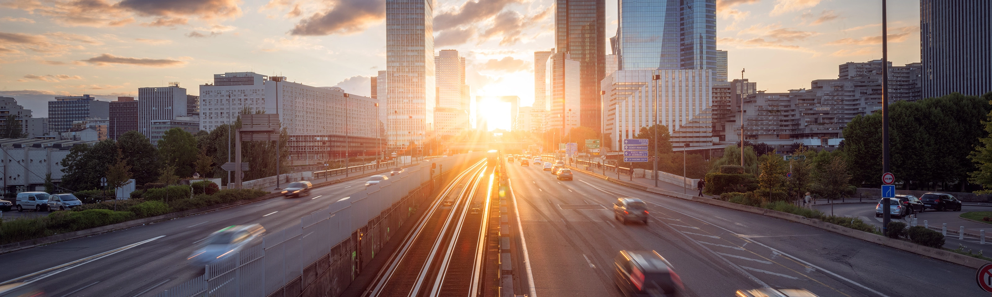Urban highway with moving cars and modern skyscrapers at sunset.