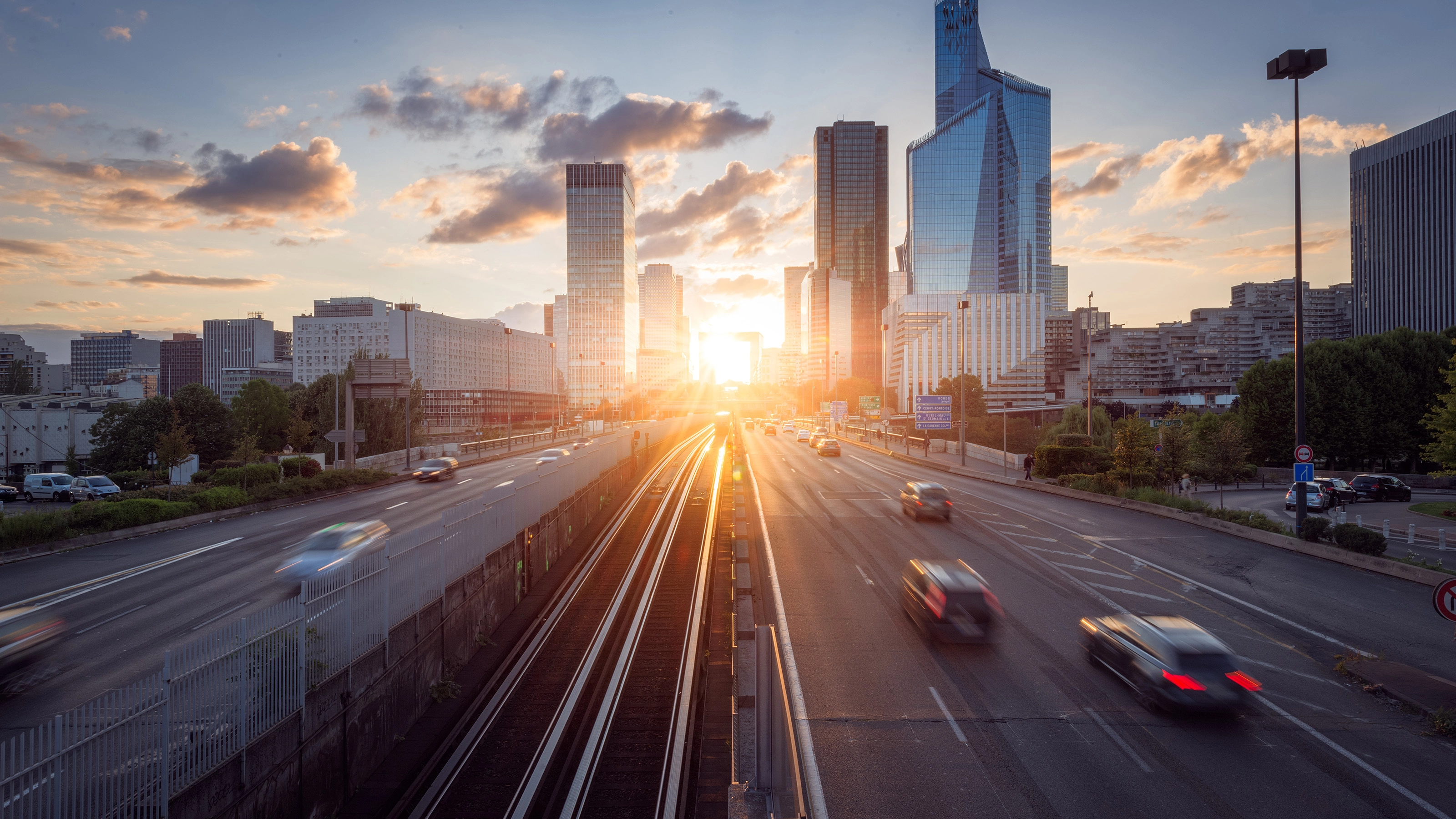 Urban highway with moving cars and modern skyscrapers at sunset.