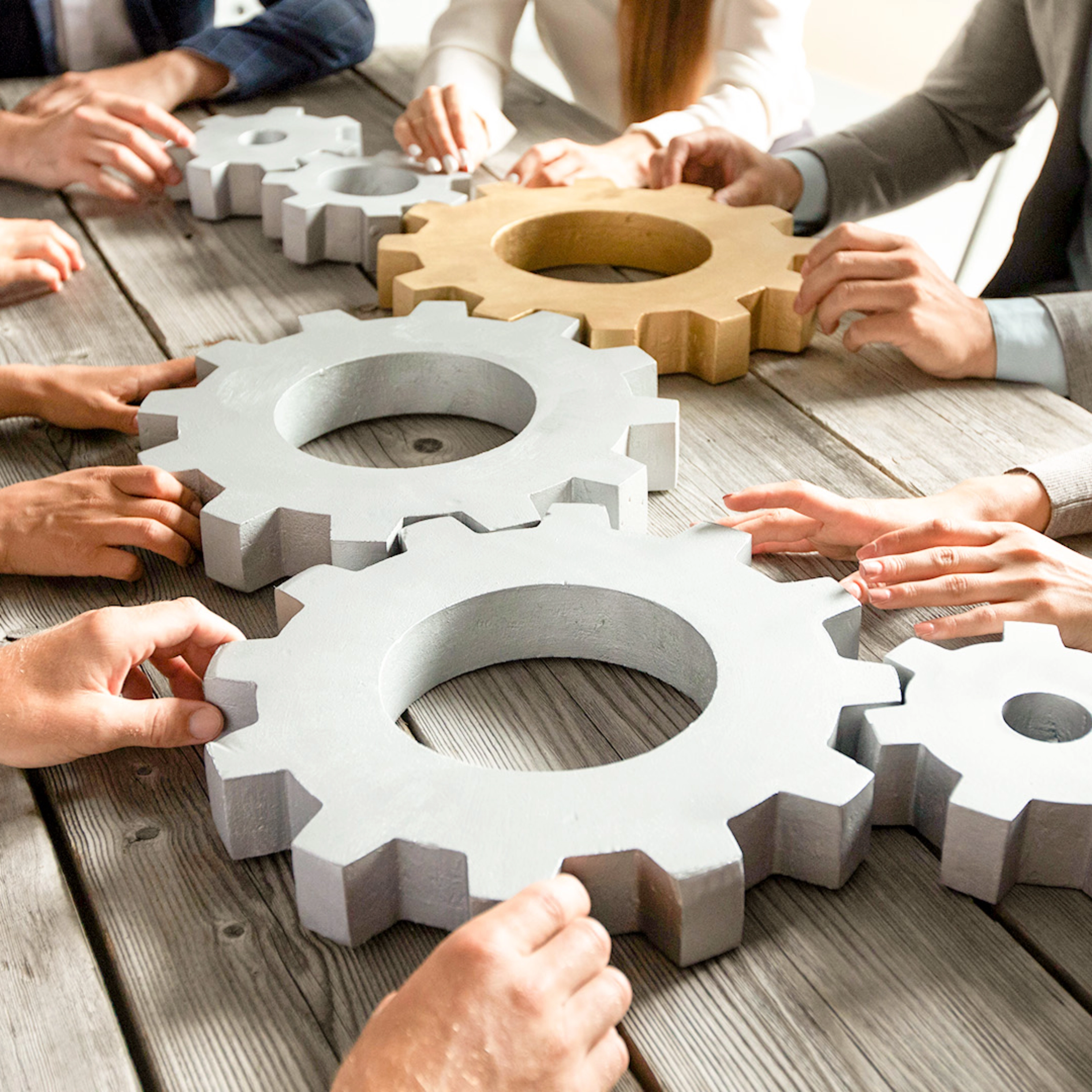 People collaboratively pushing large gears together on a wooden table.