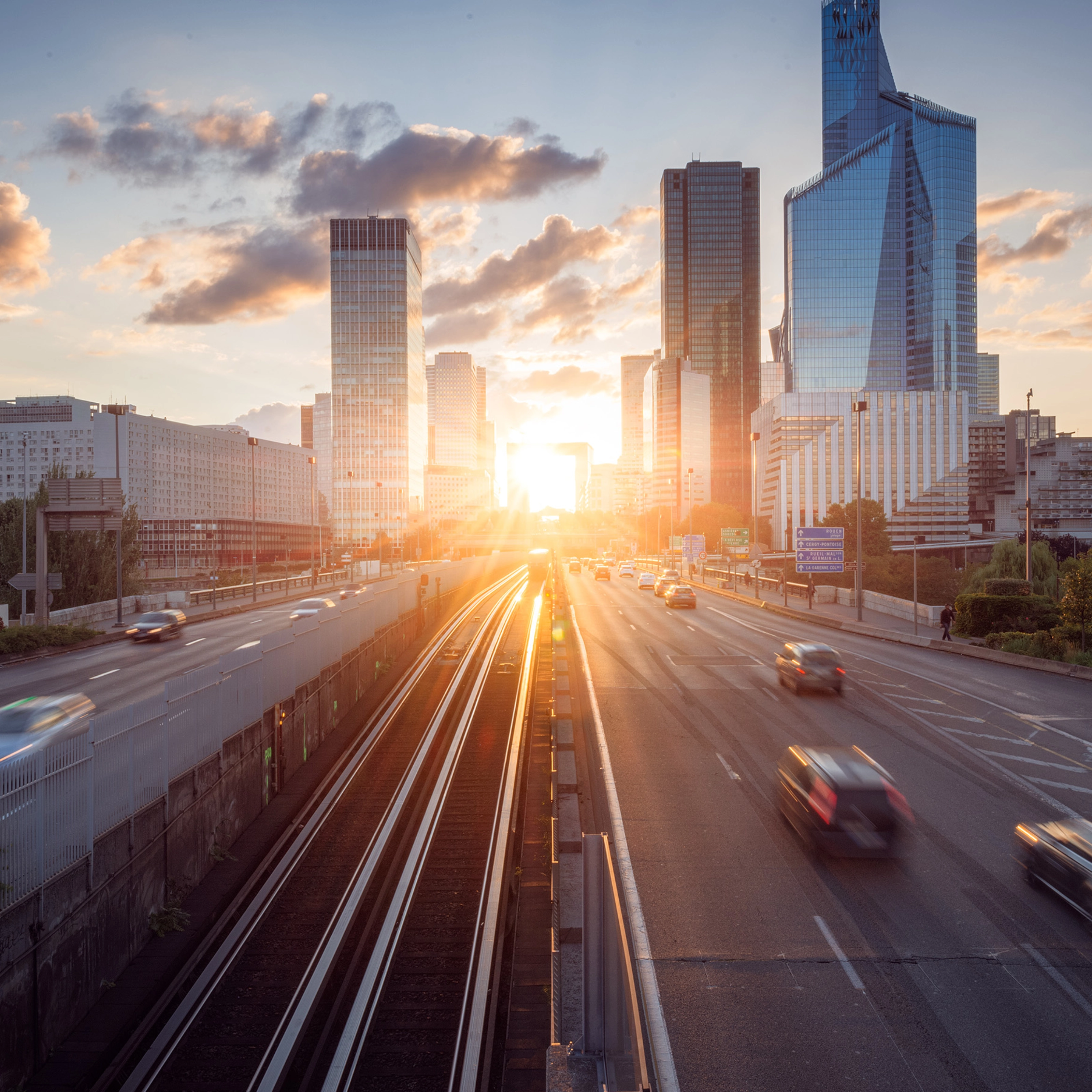 Urban highway with moving cars and modern skyscrapers at sunset.