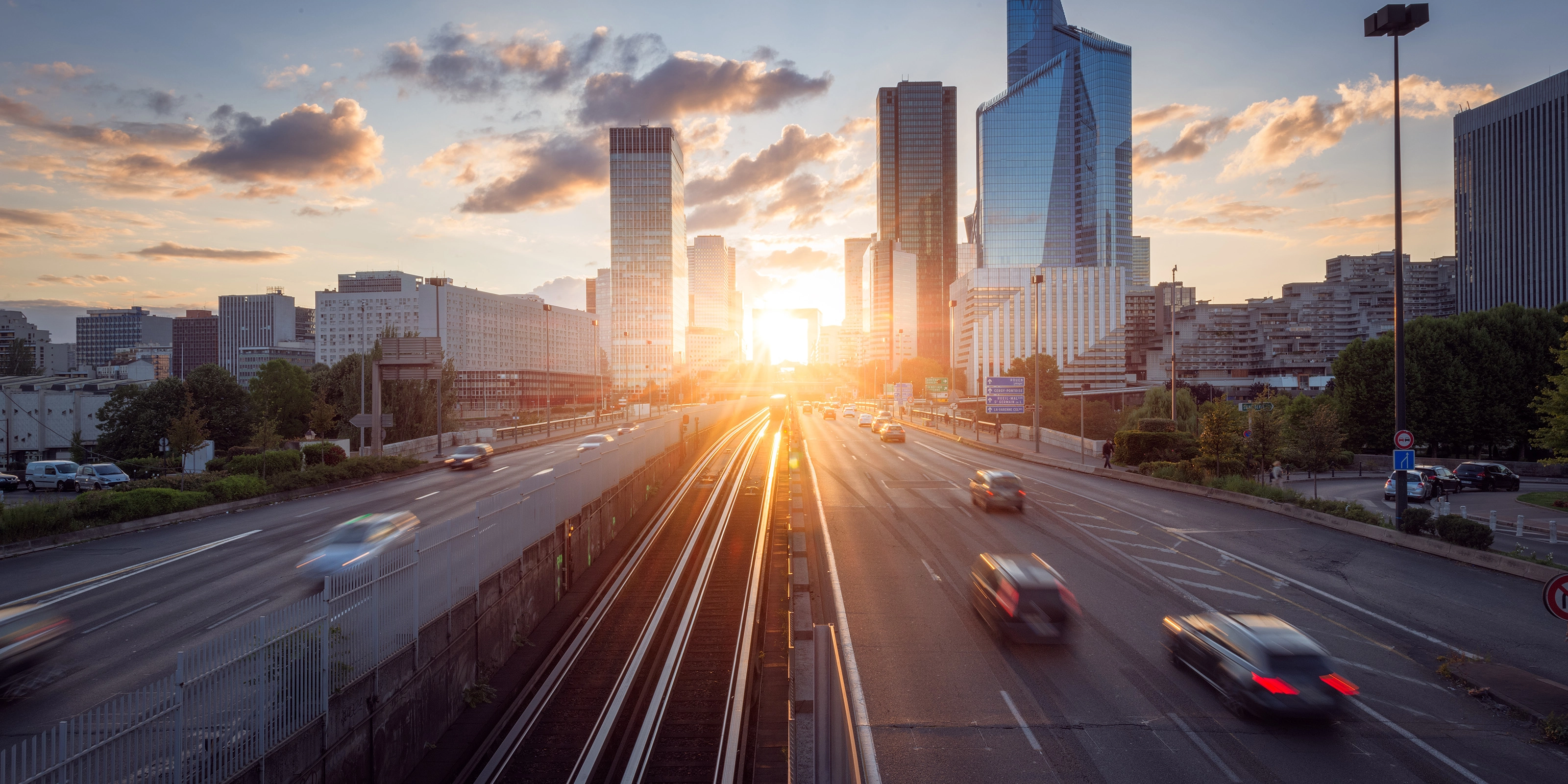 Urban highway with moving cars and modern skyscrapers at sunset.