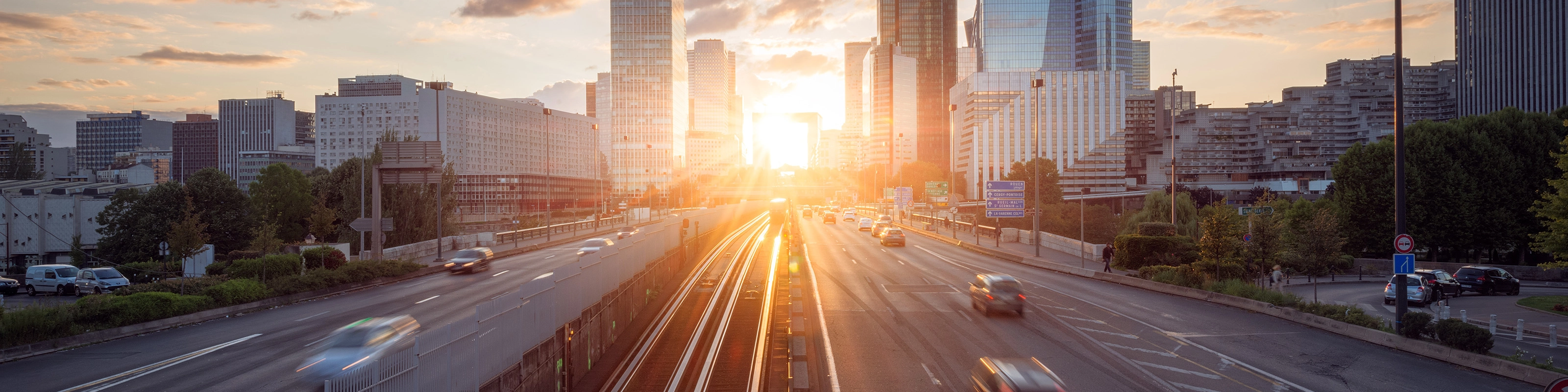 Urban highway with moving cars and modern skyscrapers at sunset.