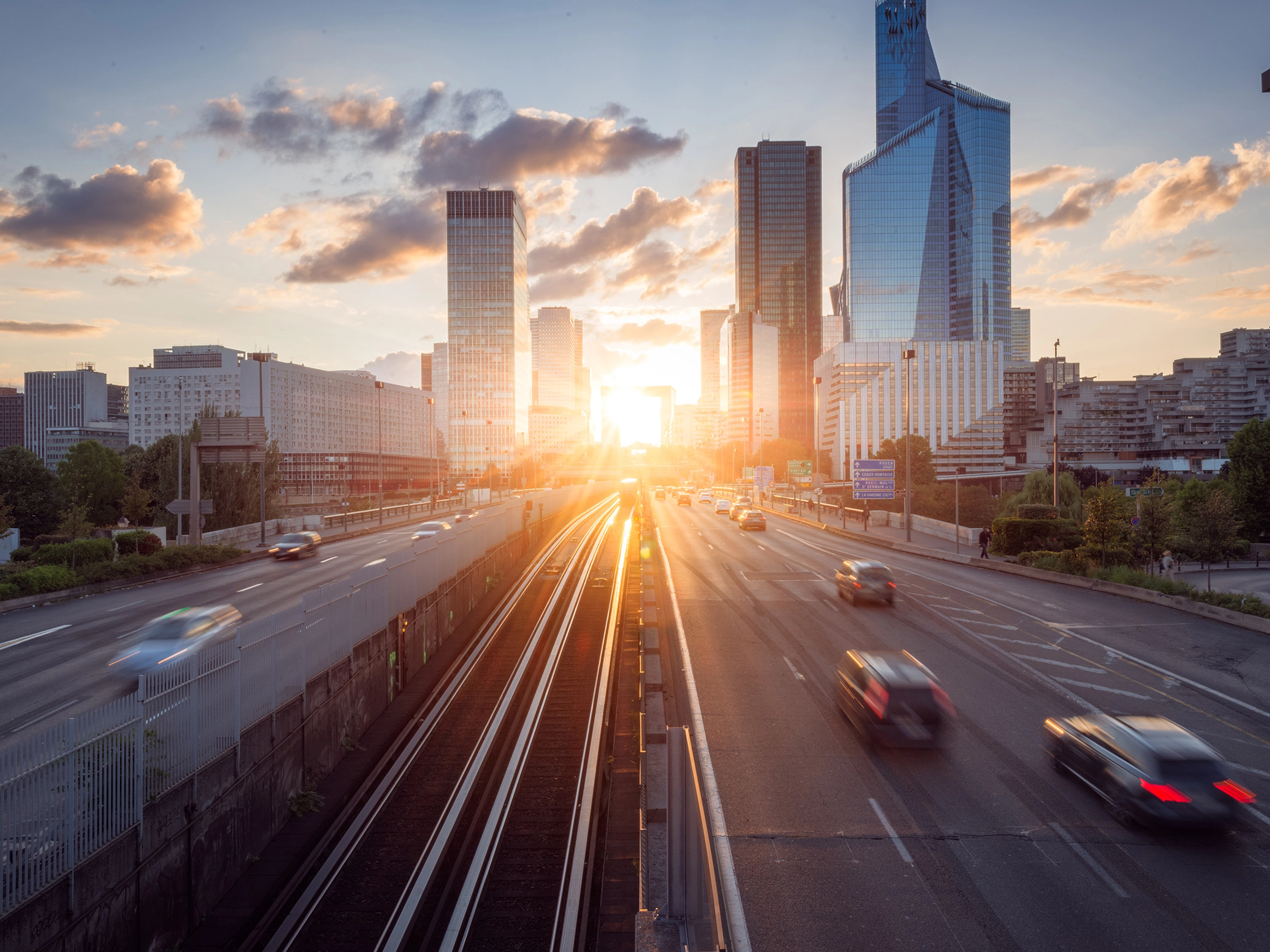 Urban highway with moving cars and modern skyscrapers at sunset.