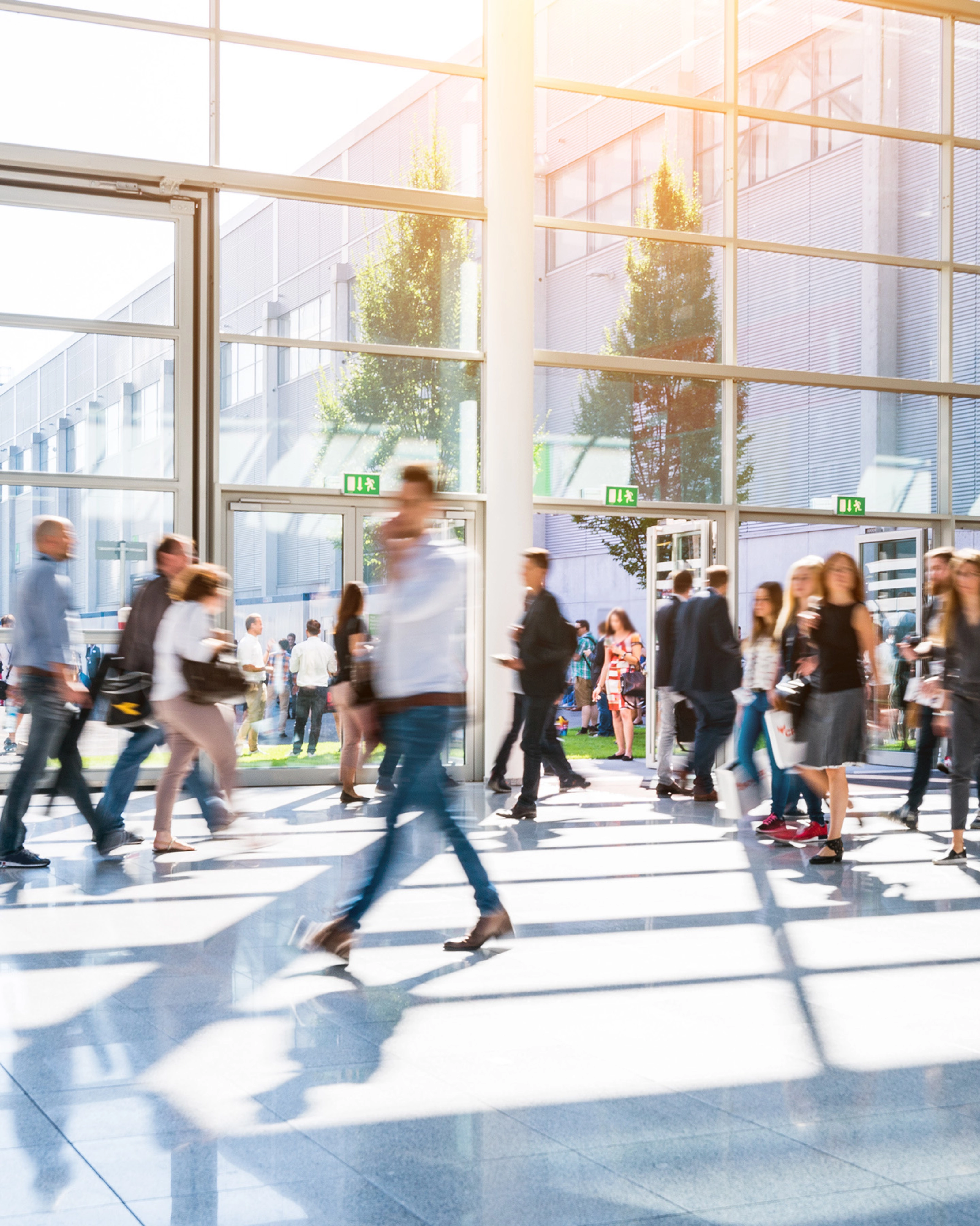 People walk through glass entrances of a modern exhibition hall in daylight.