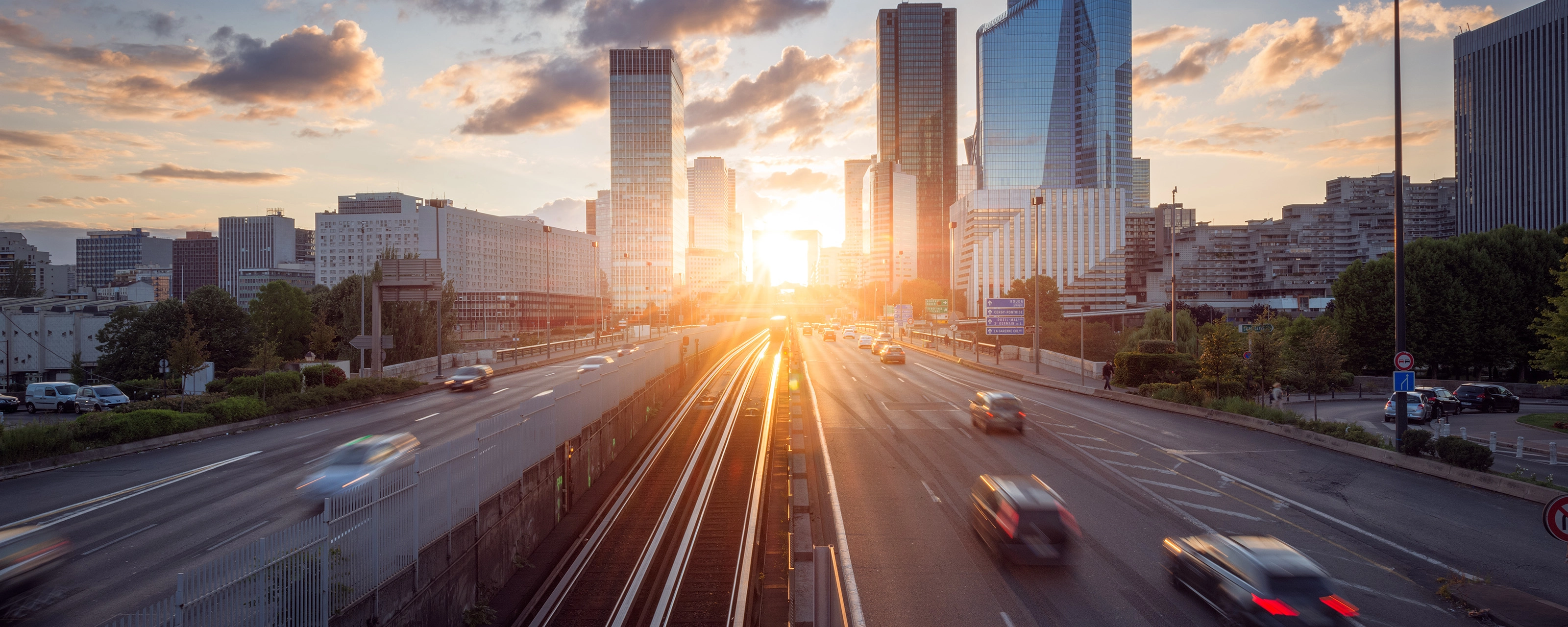 Urban highway with moving cars and modern skyscrapers at sunset.