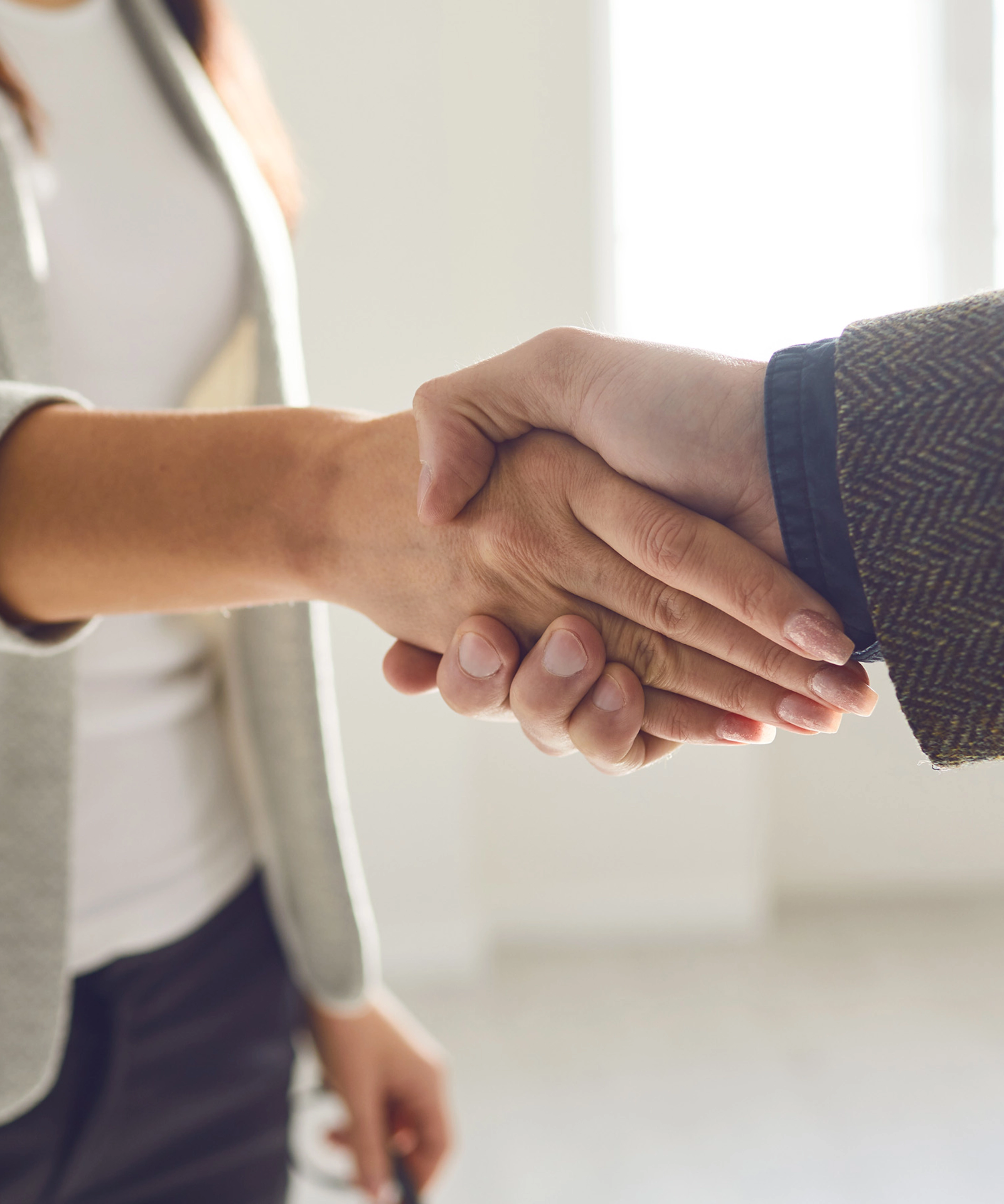 Two people in business attire shaking hands in a bright office space.