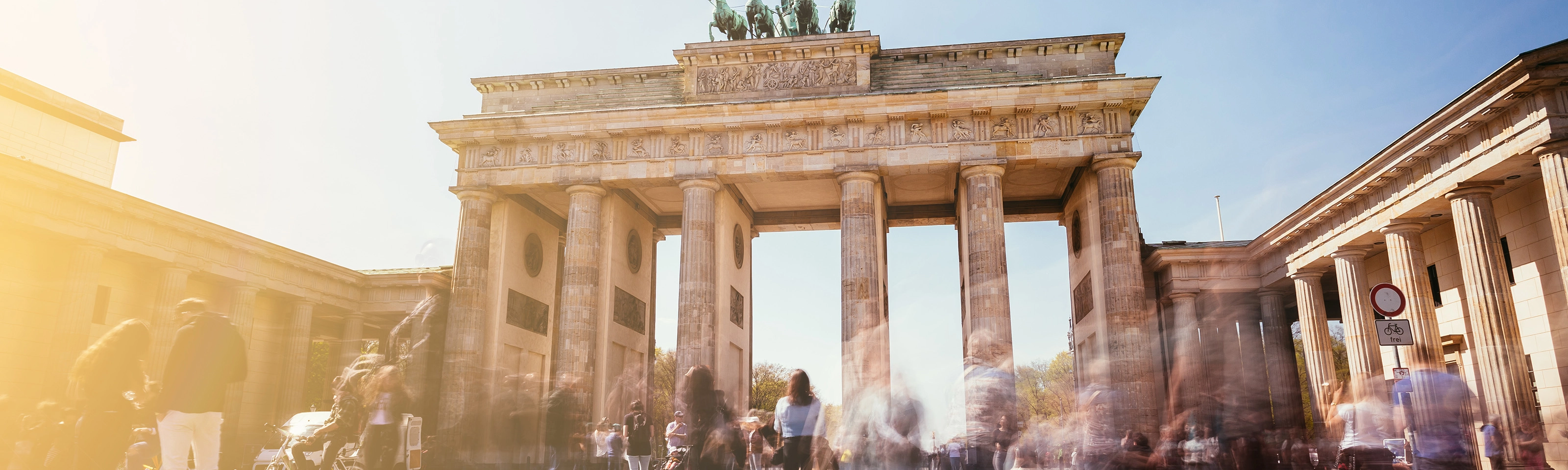 Brandenburg Gate in Berlin with many people in motion on a sunny day.