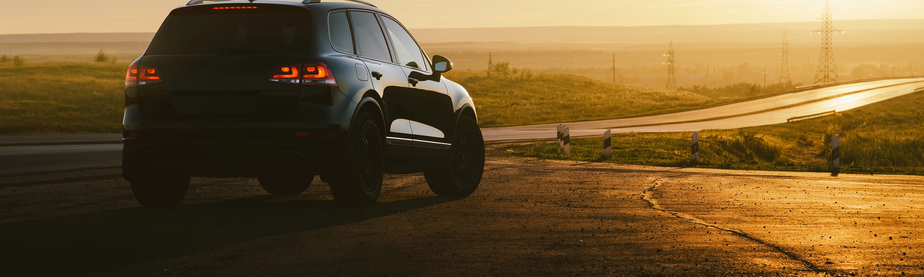 SUV on a country road at sunset with taillights illuminated.