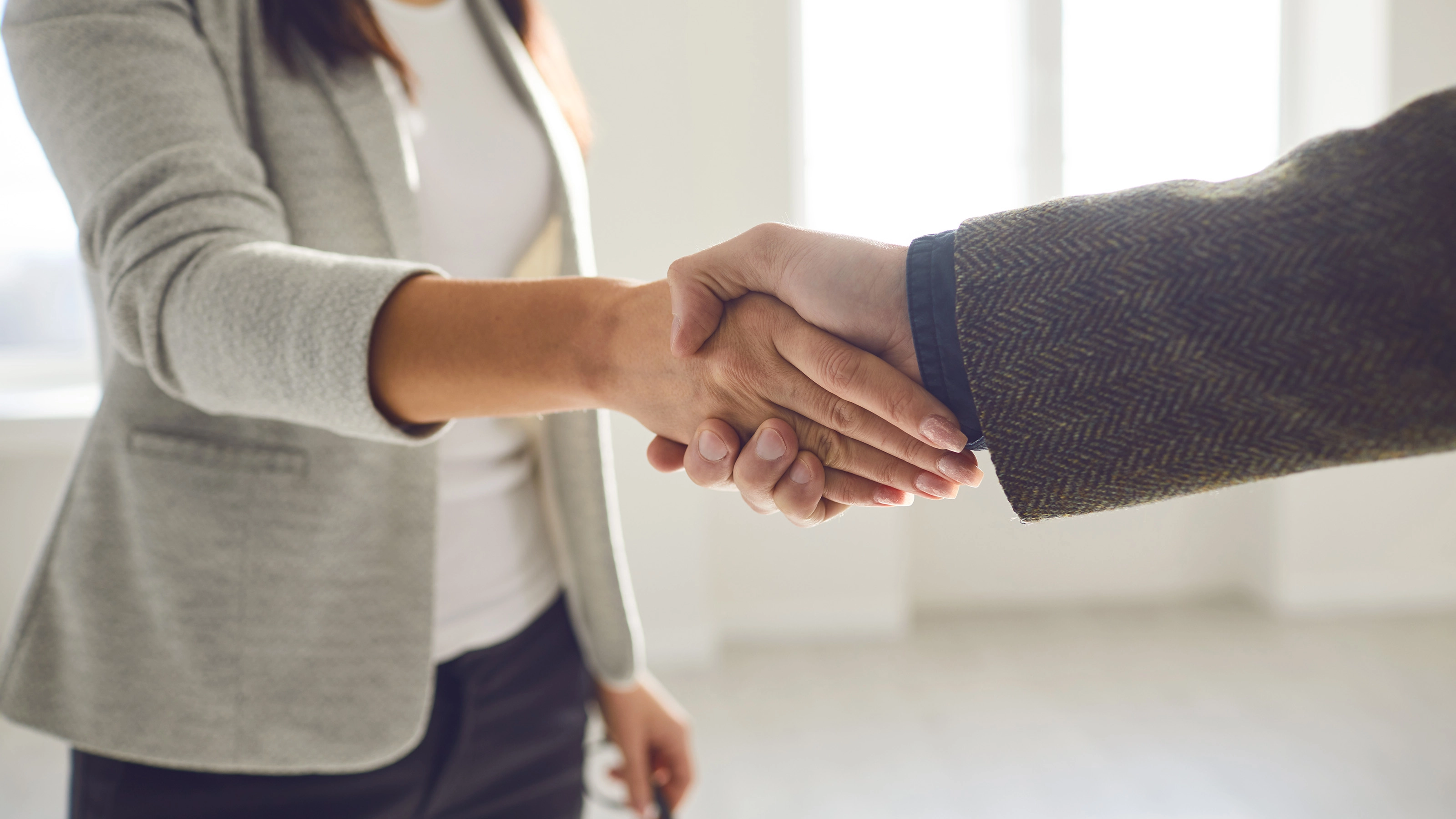 Two people in business attire shaking hands in a bright office space.