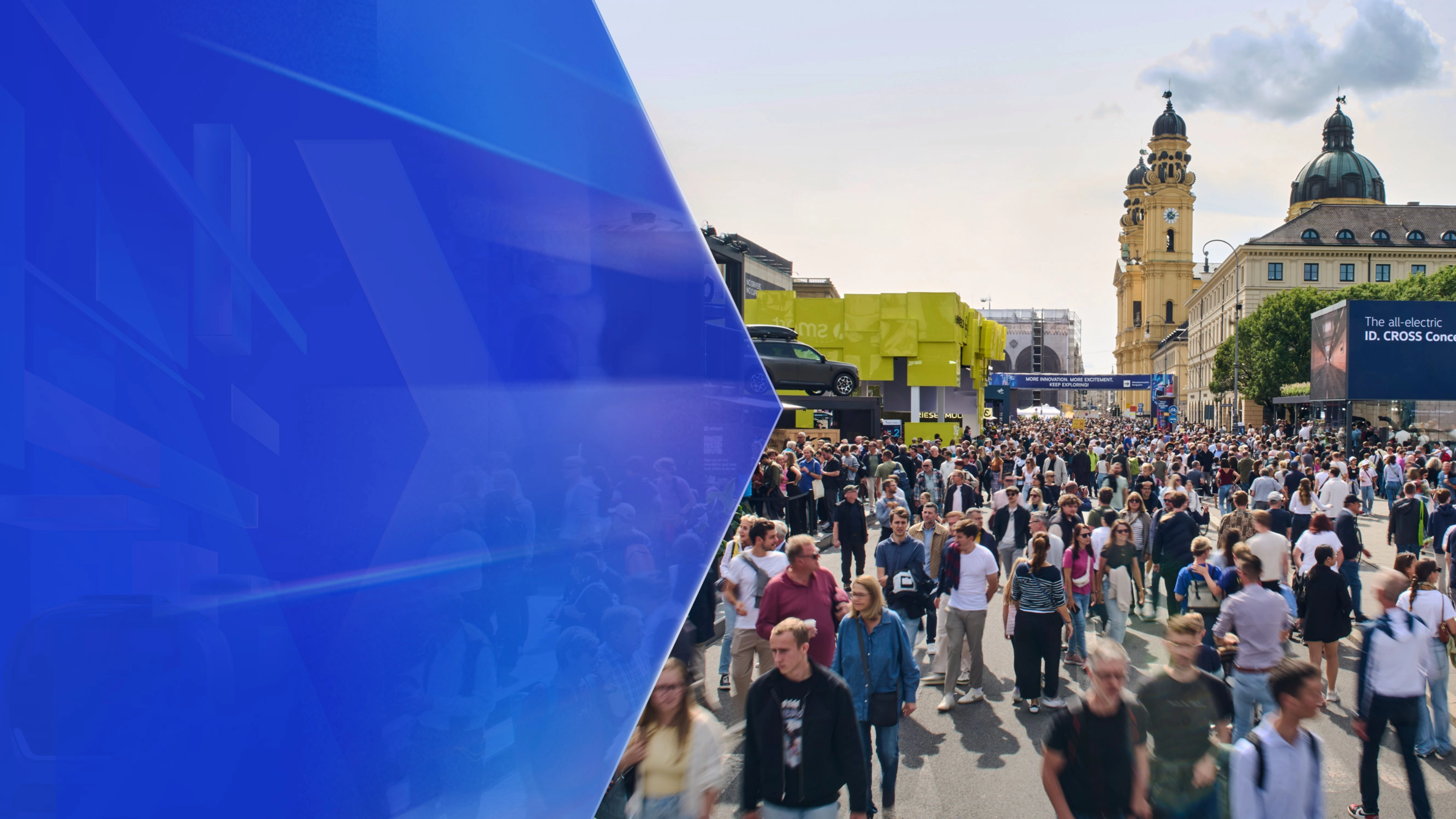 Large crowd at an outdoor mobility fair with exhibition booths and historic buildings in the background.