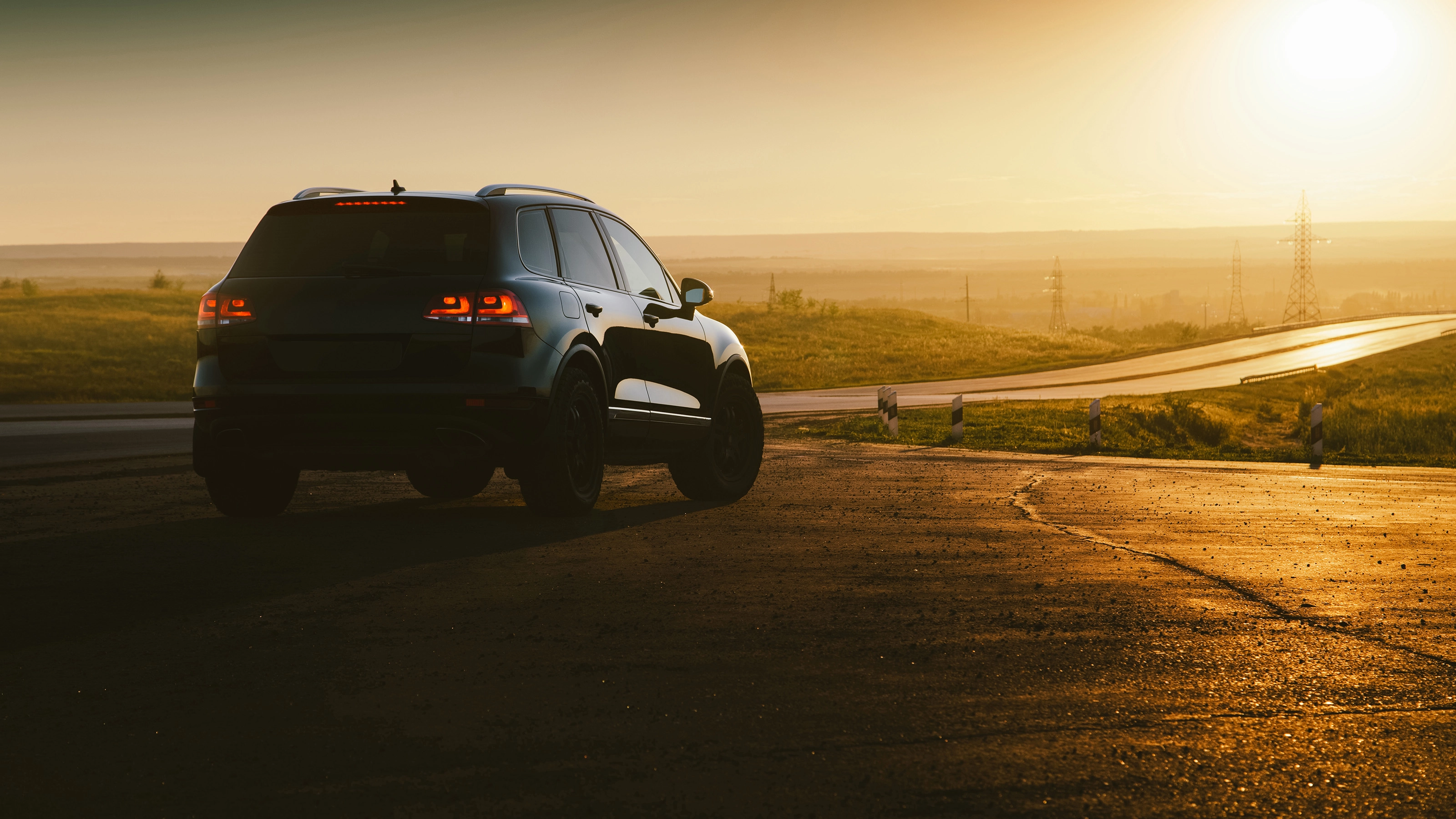 SUV on a country road at sunset with taillights illuminated.