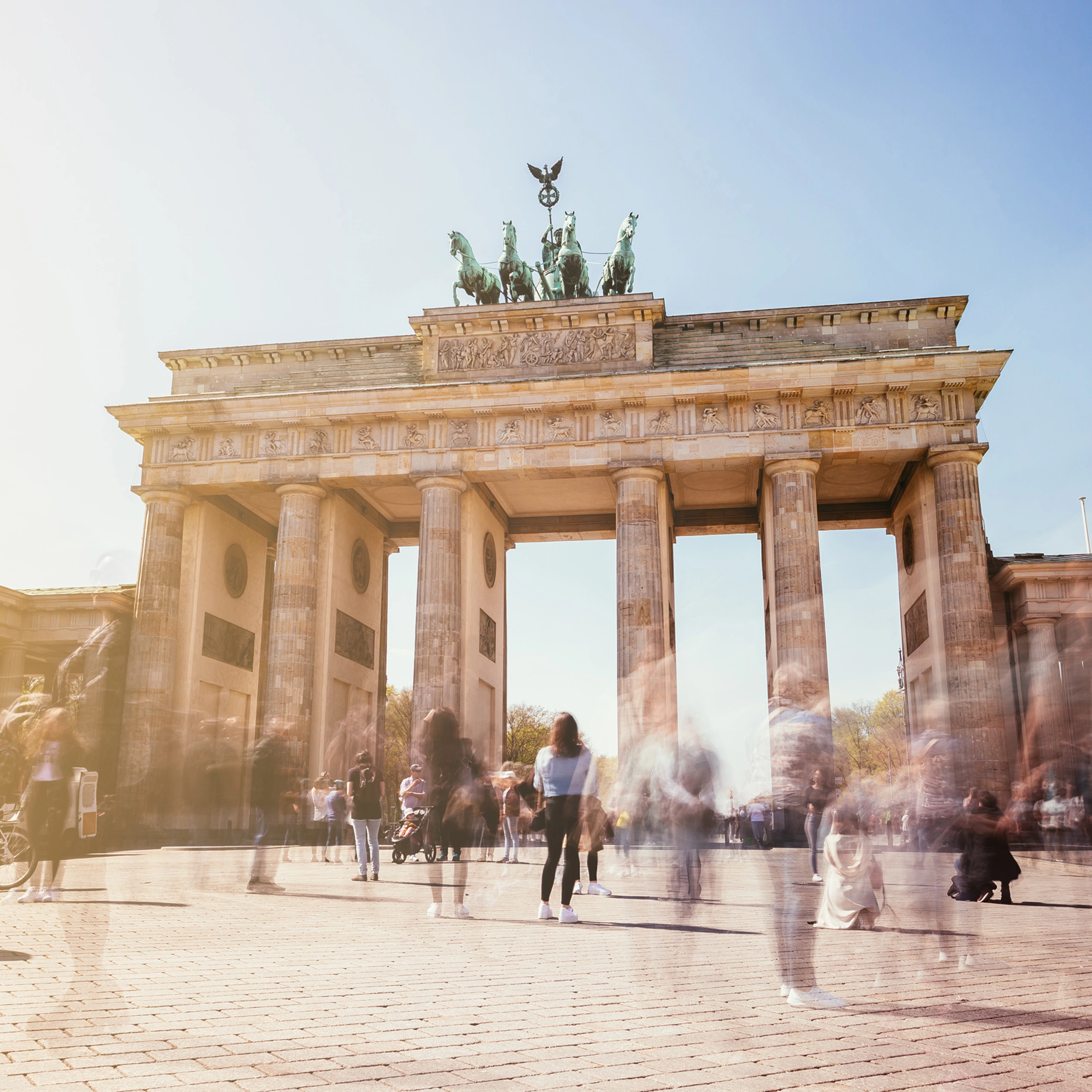 Brandenburg Gate in Berlin with many people in motion on a sunny day.