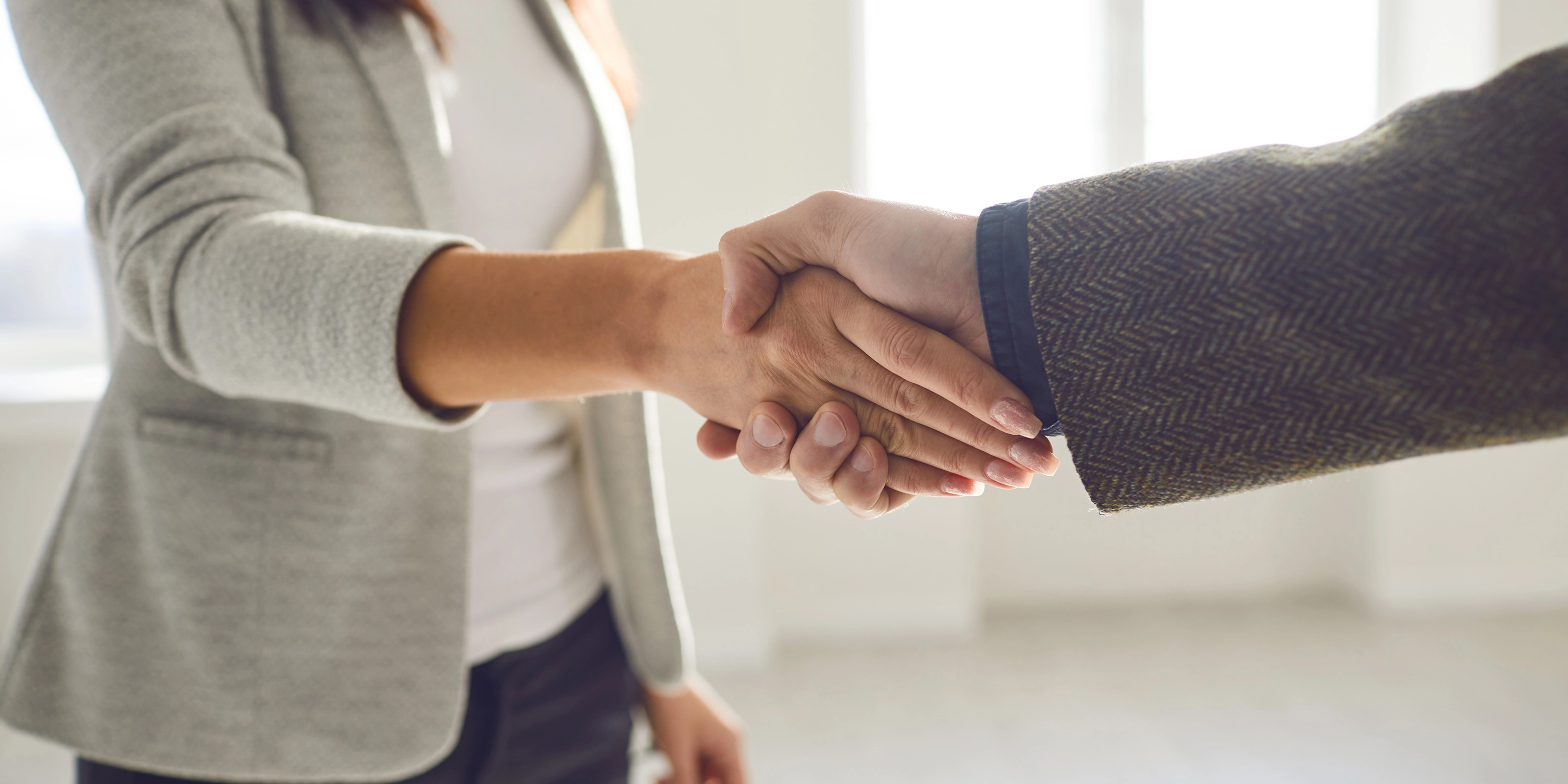 Two people in business attire shaking hands in a bright office space.
