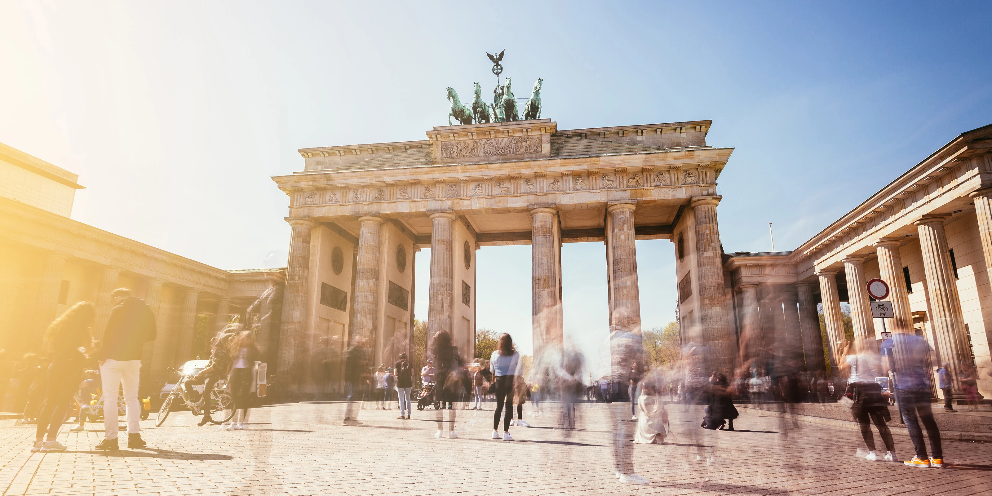 Brandenburg Gate in Berlin with many people in motion on a sunny day.