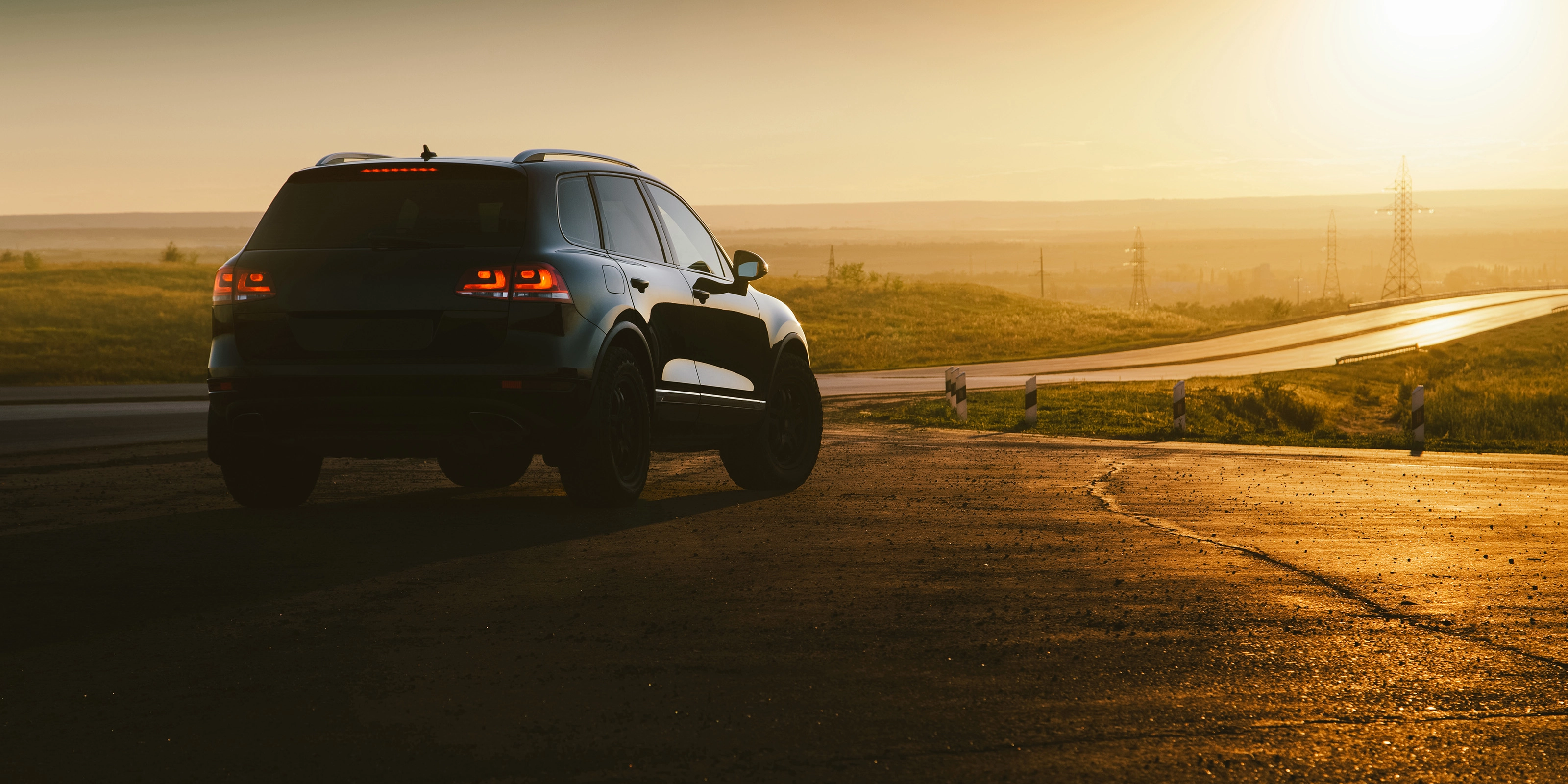 SUV on a country road at sunset with taillights illuminated.