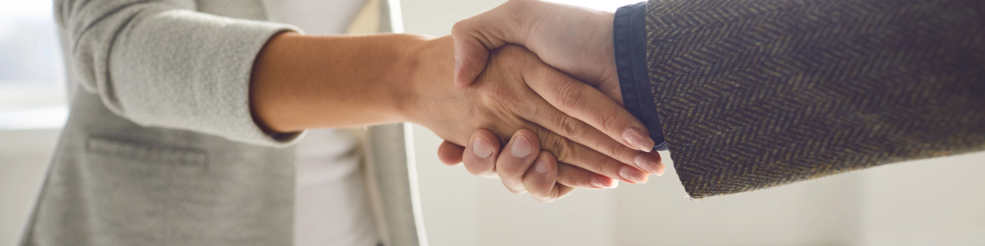 Two people in business attire shaking hands in a bright office space.