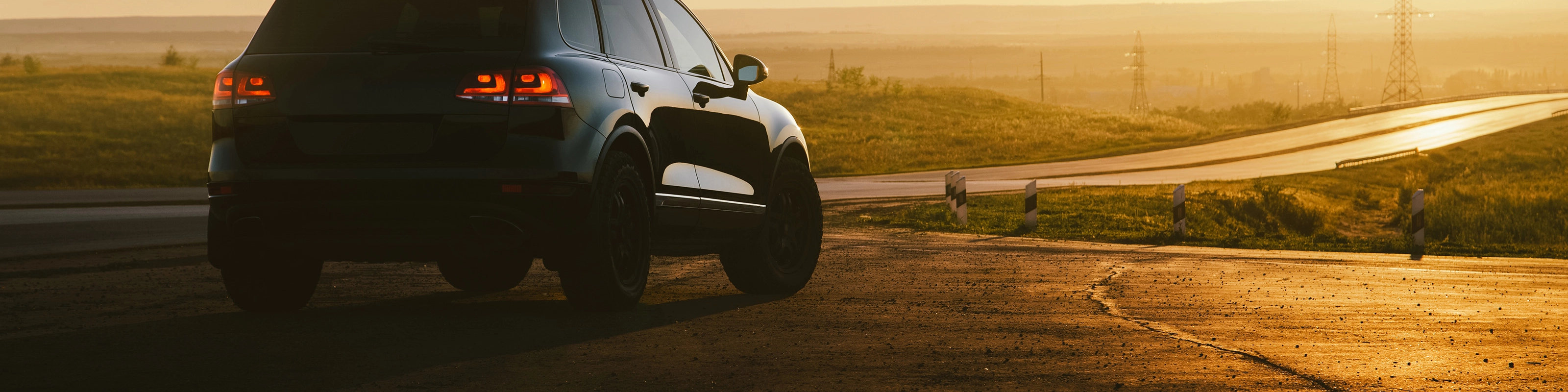 SUV on a country road at sunset with taillights illuminated.
