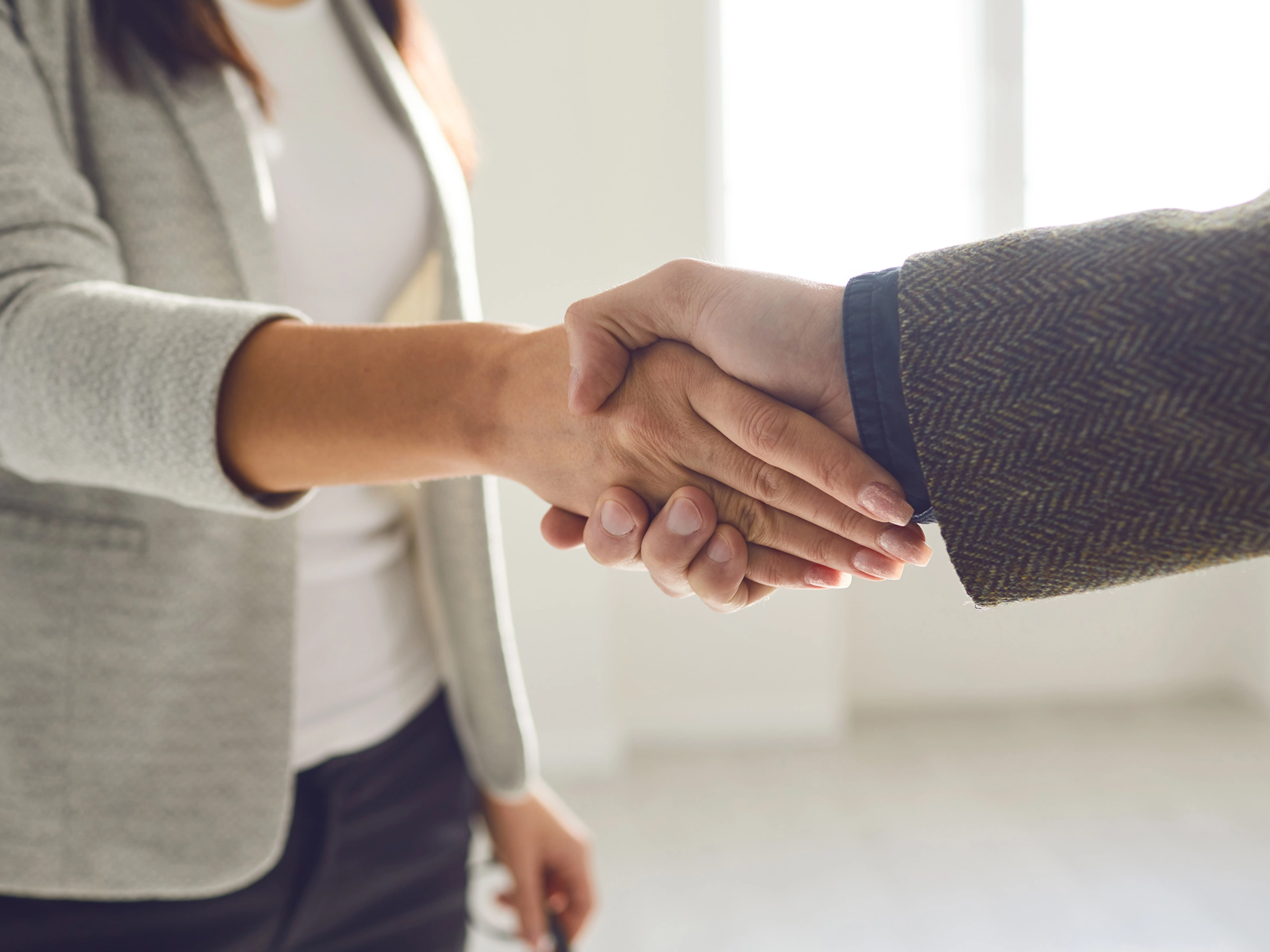 Two people in business attire shaking hands in a bright office space.