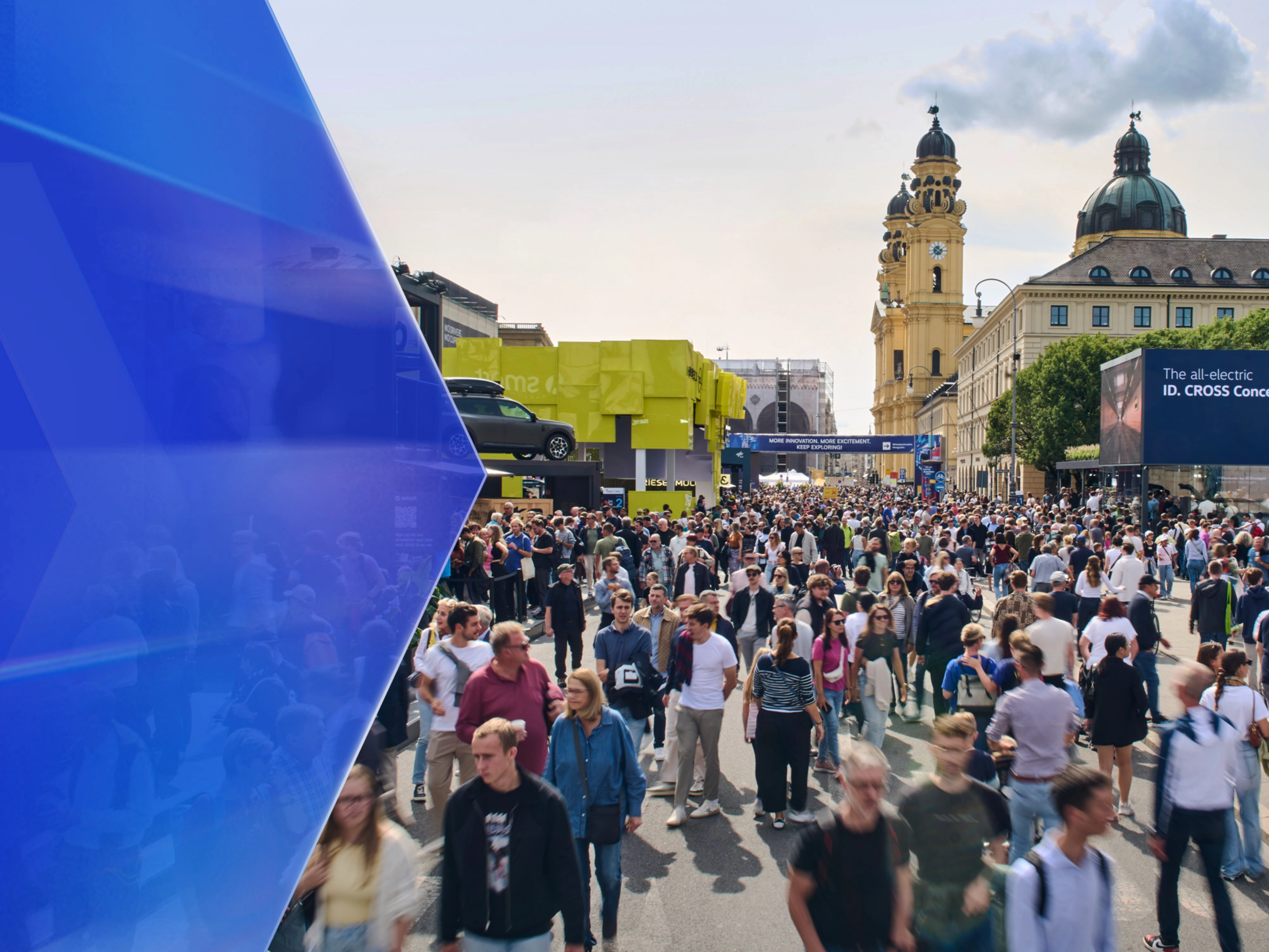 Large crowd at an outdoor mobility fair with exhibition booths and historic buildings in the background.
