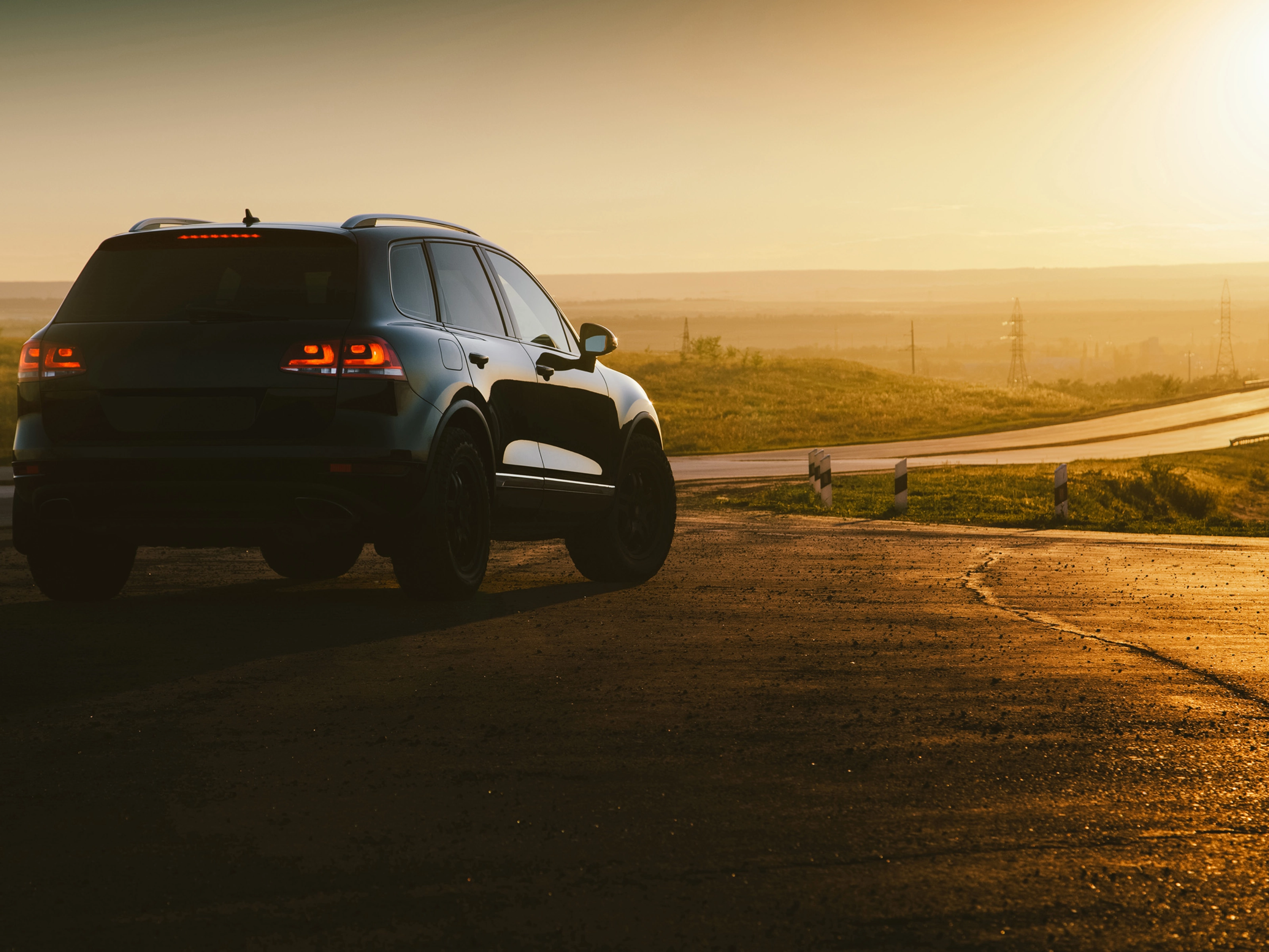 SUV on a country road at sunset with taillights illuminated.