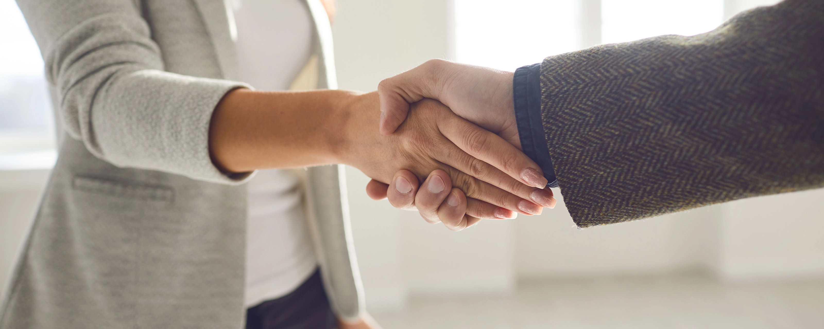 Two people in business attire shaking hands in a bright office space.