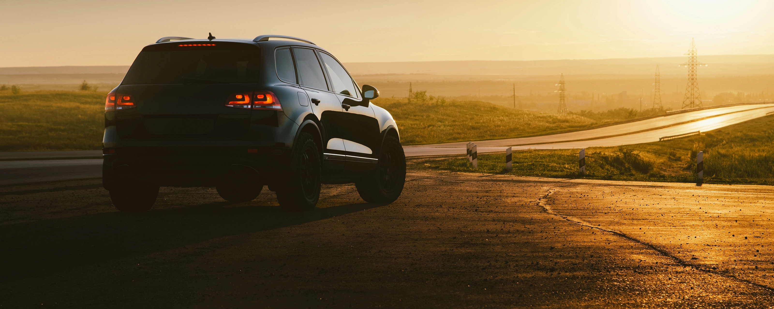 SUV on a country road at sunset with taillights illuminated.